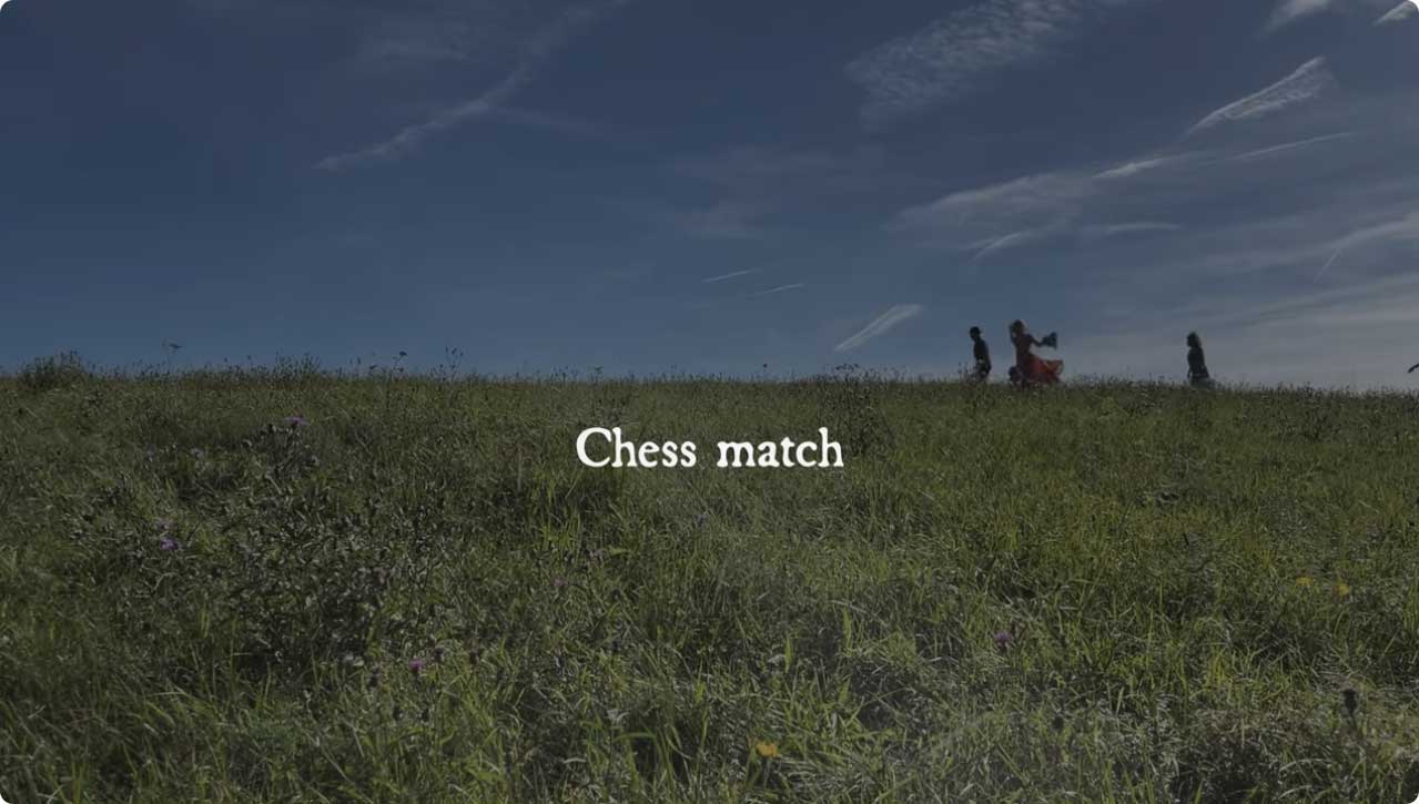 Videoscreenshot: Menschen laufen über Blumenwiese vor blauem Himmel, in der Mitte der Schriftzug "Chess Match"